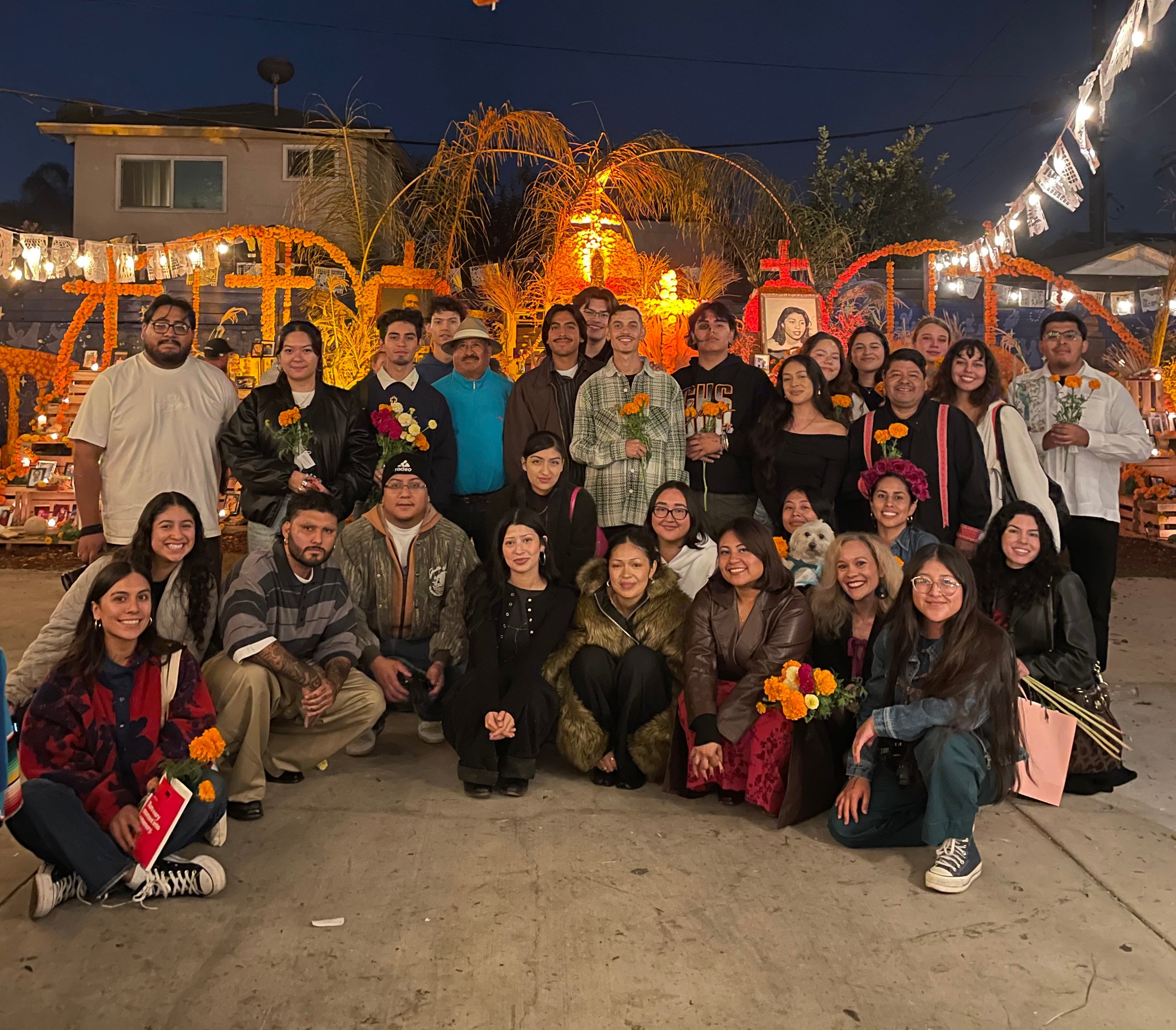 Group of people posing for a photo in front of festive decorations on a street at night.